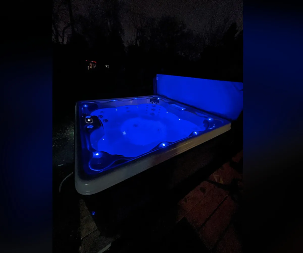 An inviting hot tub illuminated with blue lighting sits amidst dark trees, offering a serene nighttime spot for relaxation. The mood is calm and rejuvenating, perfect for unwinding after a day of adventure.