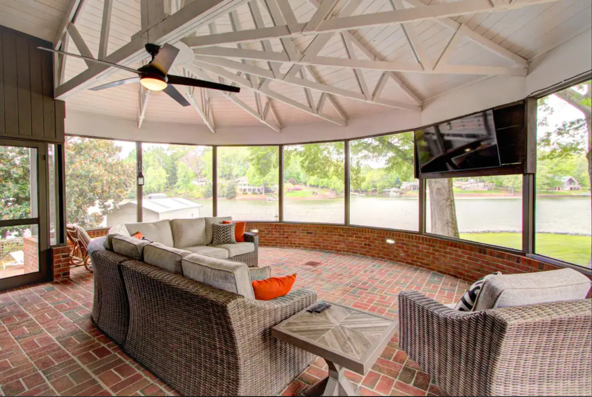 A comfortable seating area arranged to maximize views through large windows that look out over Lake Wylie. The space is designed for relaxation and socializing, with a ceiling fan and natural light enhancing the inviting atmosphere.