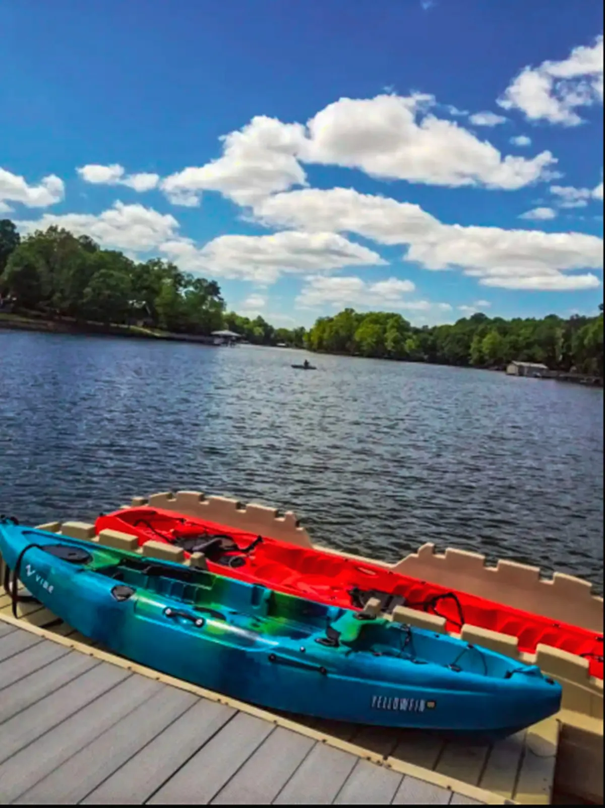 A scenic view of two colorful kayaks (blue and red) resting by calm lake waters under a cloudy sky. The dock provides easy water access, suggesting opportunities for kayaking, fishing, or enjoying peaceful moments by the lake.