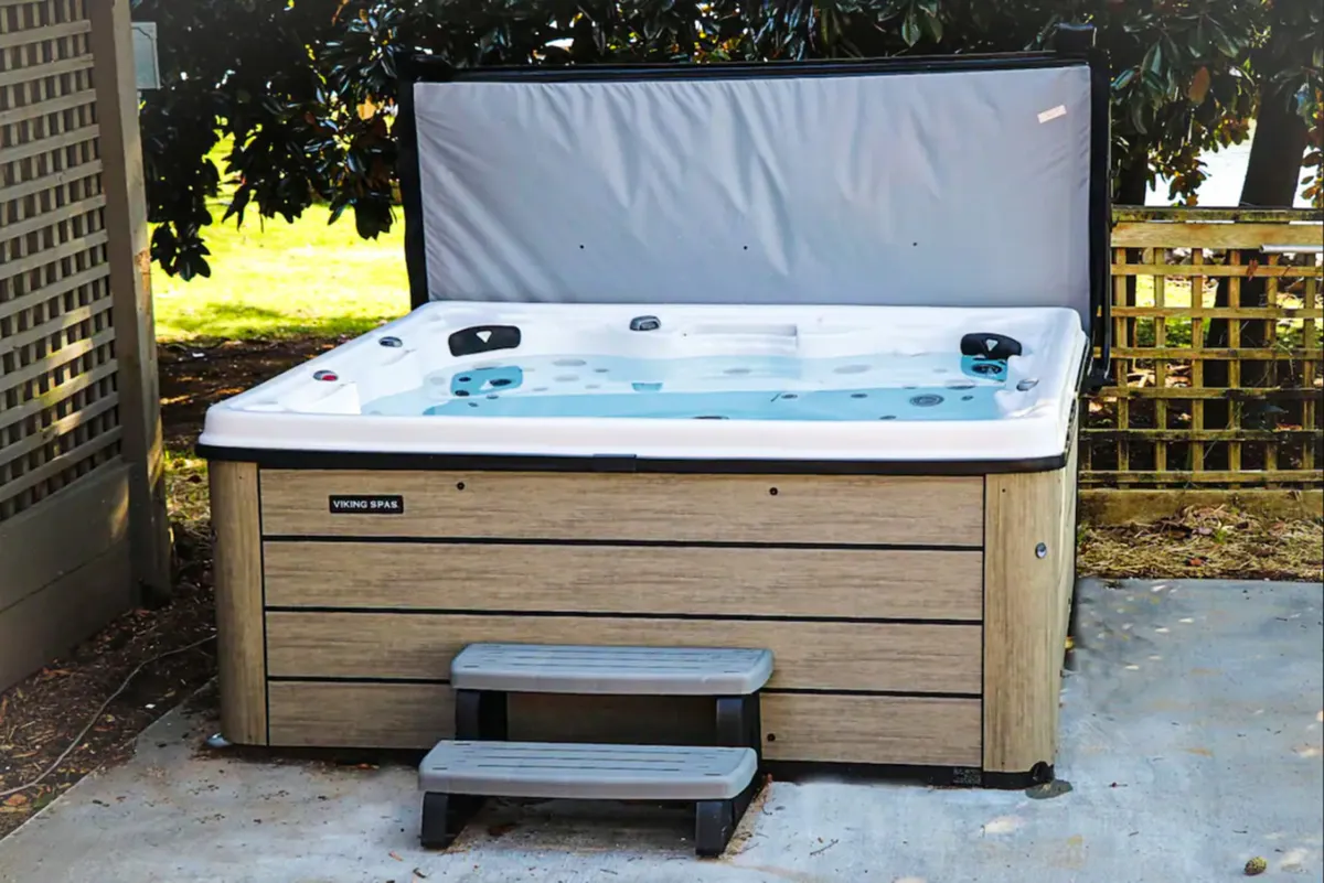 A cozy hot tub nestled outdoors with steps leading up, surrounded by greenery, inviting groups to relax together and unwind. The tranquil atmosphere makes it perfect for evening soaks or celebrations with friends.